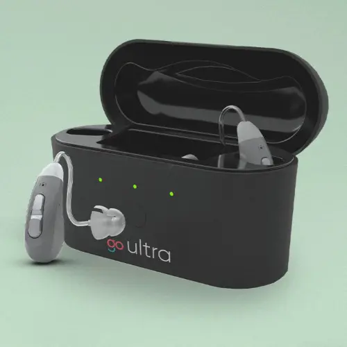 Gray Go Hearing hearing aids in a black charging case against a green background.
