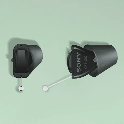 Black Sony in-the-ear hearing aids isolated on a green background with a shadow