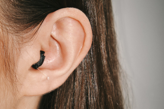 A Black Sony hearing aid worn in a white woman’s ear