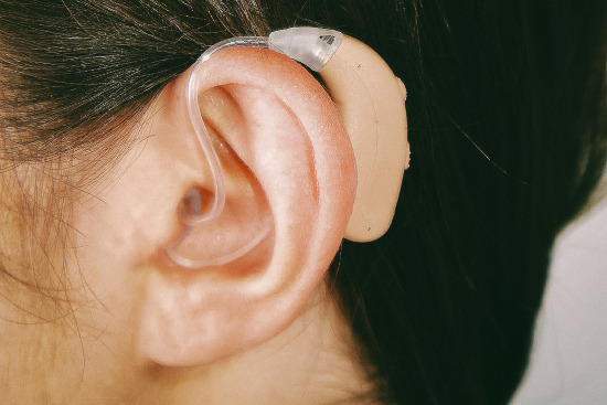A beige MDHearing hearing aid close-up in a white woman’s ear.