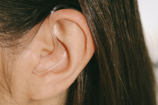 A white woman wears a Go Hearing hearing aid in her left ear.