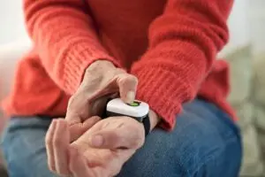 An older adult wearing red sweater pushes medical alert help button on wrist