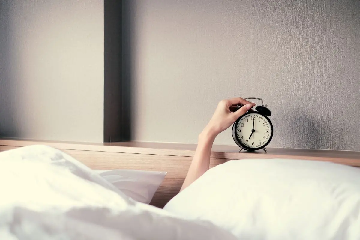 Hand reaching out of bed to turn off alarm clock